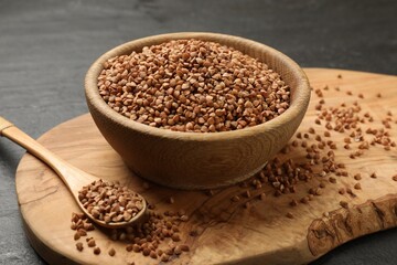 Bowl and spoon with dry buckwheat on black table, closeup