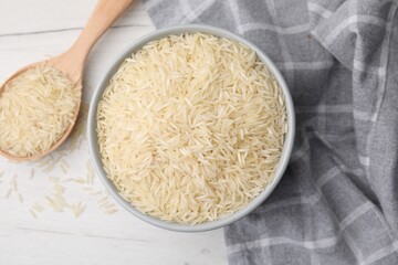 Bowl and spoon with raw rice on white wooden table, flat lay