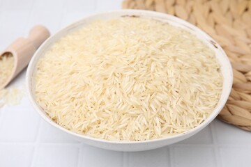 Raw rice in bowl on white tiled table, closeup