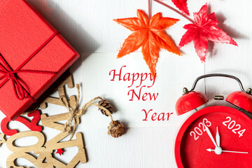 Happy New Year writing on paper note.  2023 and 2024 on red alarm clock on Christmas item. Merry...