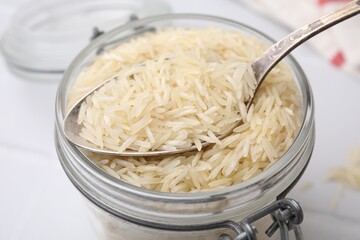 Glass jar and spoon with raw rice on table, closeup