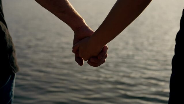 Couple in love holding hands at sunset on the river bank close-up