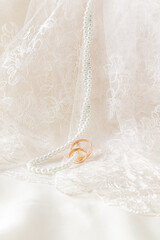 Retro beige tulle and long pearl beads hang along the soft folds of fabric with gold wedding rings...