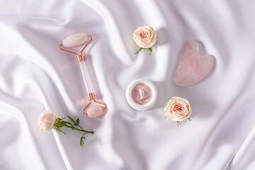 Set of cosmetics and tools on white satin background with live rosebuds. Top view. Cosmetic...