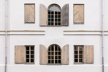.White building wall with many arched windows and wooden shutters on it