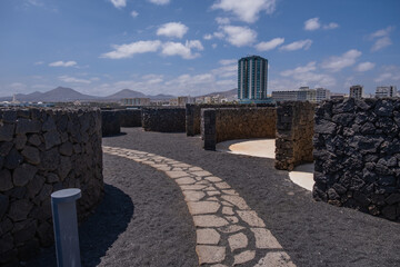 View of the city of Arrecife from the Fermina islet. Turquoise blue water. Rock structure for sunbathing. Sky with big white clouds. Seascape. Lanzarote, Canary Islands, Spain.