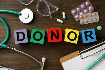 Word Donor made of colorful cubes, pills, clipboard and stethoscope on wooden table, flat lay