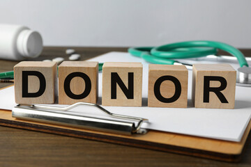 Word Donor made of cubes, clipboard and stethoscope on wooden table, closeup