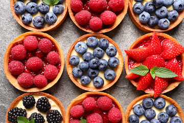 Tartlets with different fresh berries on light grey table, flat lay. Delicious dessert