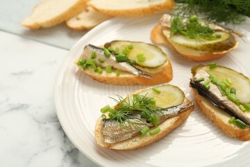 Delicious sandwiches with sprats, pickled cucumber, green onion and dill on white marble table, closeup. Space for text