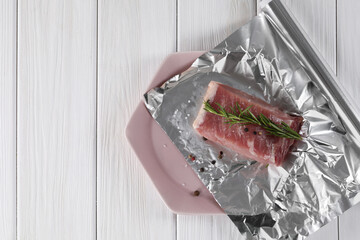 Baking pork. Aluminum foil with raw meat, rosemary and spices on white wooden table, top view