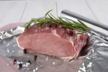 Aluminum foil with raw meat, rosemary and spices on white table, closeup