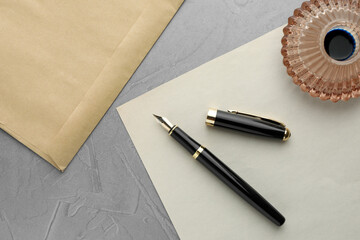 Stylish fountain pen, inkwell, envelope and paper on grey textured table, flat lay