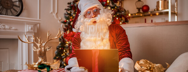 Surprised Santa Claus with glowing gift near christmas tree. New year and Merry Christmas concept