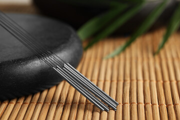 Acupuncture needles and spa stone on bamboo mat, closeup