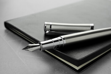 Stylish fountain pen, cap and leather notebook on light grey textured table, closeup - obrazy, fototapety, plakaty