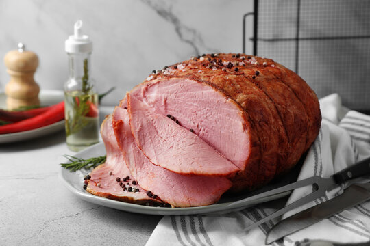 Delicious baked ham, carving fork and knife on light grey table