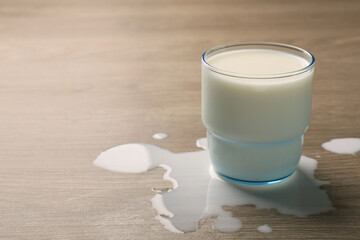 Spilled milk and glass of drink on wooden table. Space for text