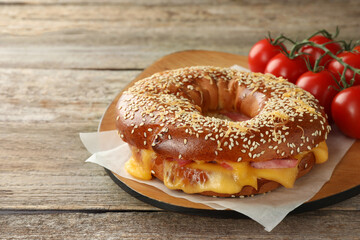 Delicious bagel with ham, cheese and tomatoes on wooden table, space for text