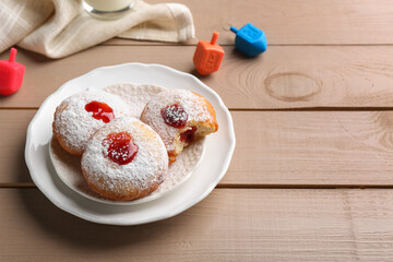 Hanukkah donuts and dreidels on wooden table, space for text