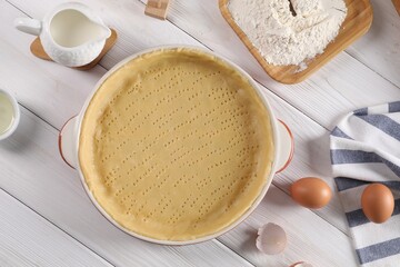 Pie tin with fresh dough and ingredients on white wooden table, flat lay. Making quiche