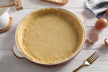 Pie tin with fresh dough and ingredients on white wooden table. Making quiche