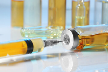 Filling syringe with orange medication from glass vial on white table, closeup