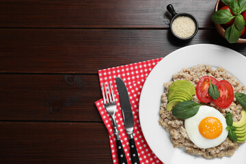 Delicious boiled oatmeal with fried egg, tomato and avocado served on wooden table, flat lay. Space for text