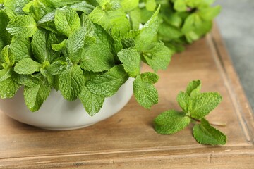 Bowl with fresh green mint leaves on wooden board, closeup