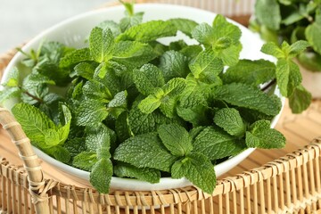 Bowl of fresh green mint leaves on wicker tray, closeup