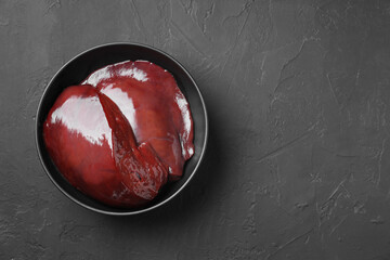 Pieces of raw beef liver in bowl on black table, top view. Space for text