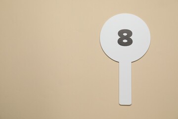 Auction paddle with number 8 on beige background, top view. Space for text