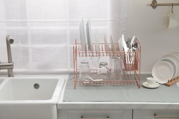 Drying rack with clean dishes on countertop near sink in kitchen