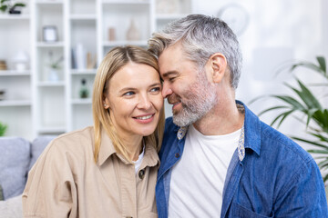 Romantic happy middle age couple relaxing on sofa at home, smiling, loving mature couple relaxing in cozy living room interior, cuddling on sofa, enjoying weekend together, copy space.