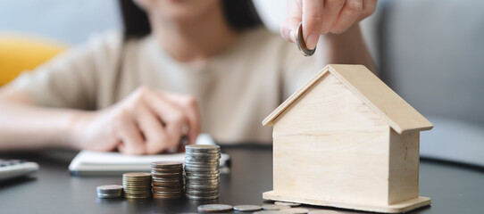 Close up hands of Woman putting coin into piggy bank house model  saving for buy property