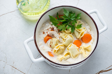 Bowl of creamy soup with italian tortellini and chicken fillet, high angle view on a white granite background, horizontal shot