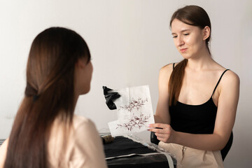 female tottooist showing sketch of a tattoo to her client in the office