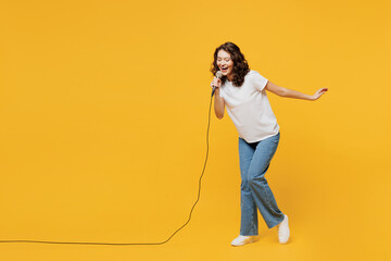 Full body singer happy fun young woman wear white blank t-shirt casual clothes sing song in microphone at karaoke club isolated on plain yellow orange background studio portrait. Lifestyle concept. - obrazy, fototapety, plakaty