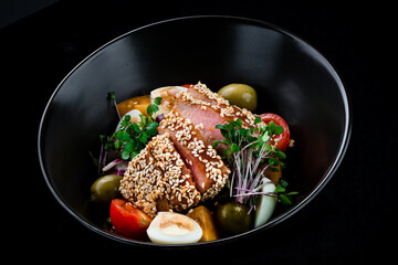 Salad with raw tuna, cherry tomatoes, olives, quail eggs and microgreens in a dark background.