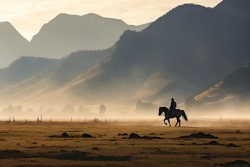 Fototapeten Landscape photography capturing a peaceful scene of a rider and horse against a mountain backdrop, enveloped in early morning mist, evoking tranquility. © Kristian