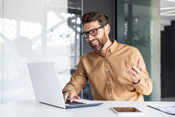 Online video call, remote conversation, man smiling at presentation talking to colleagues and partners, businessman working inside office with laptop, wearing shirt and glasses - obrazy, fototapety, plakaty