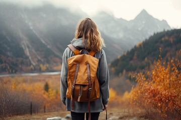 Young woman with backpack enjoying an adventurous hike in nature while admiring the breathtaking view from a mountain peak at sunset. - obrazy, fototapety, plakaty