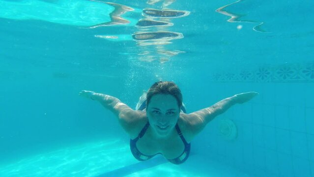 A girl swims underwater in a blue pool with her eyes open