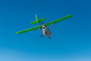 Ultralight single-propeller plane with skis flying over the blue sky in a winter