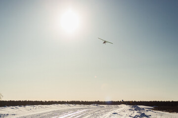 Ultralight single-propeller plane with skis flying over the blue sky in a winter