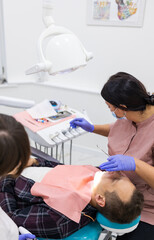 Side view of female dentist examining male patient with tools in dental clinic
