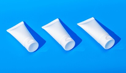 Cream tubes mockup row, three cosmetic product packages, blank white containers on blue background