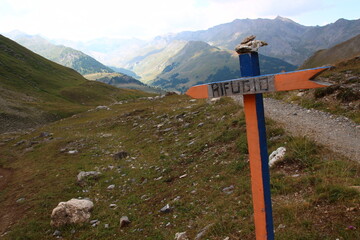 Overlooking the Lauzanier valley, a handcrafted signpost indicates a nearby shelter in Italian...