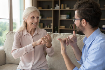 Grown up son communicates with mature retired mother using gestures. Mature woman with hearing...