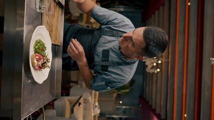 vertical video chef prepares bruschetta with beef, avocado, puts microgreens with tongs on a dish in a professional kitchen in an Italian restaurant